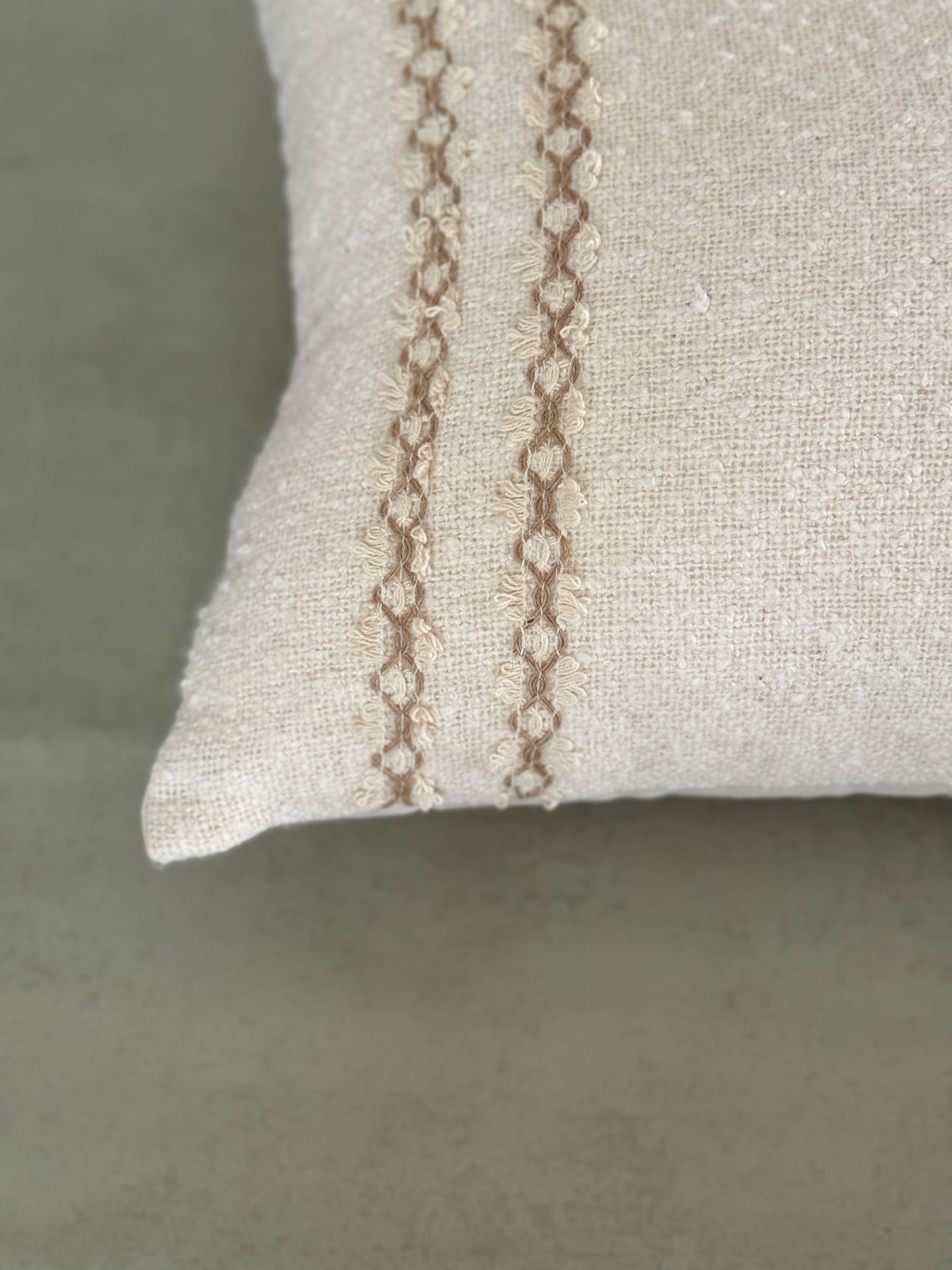 Close up of a textured ivory oblong cushion with decorative lace.