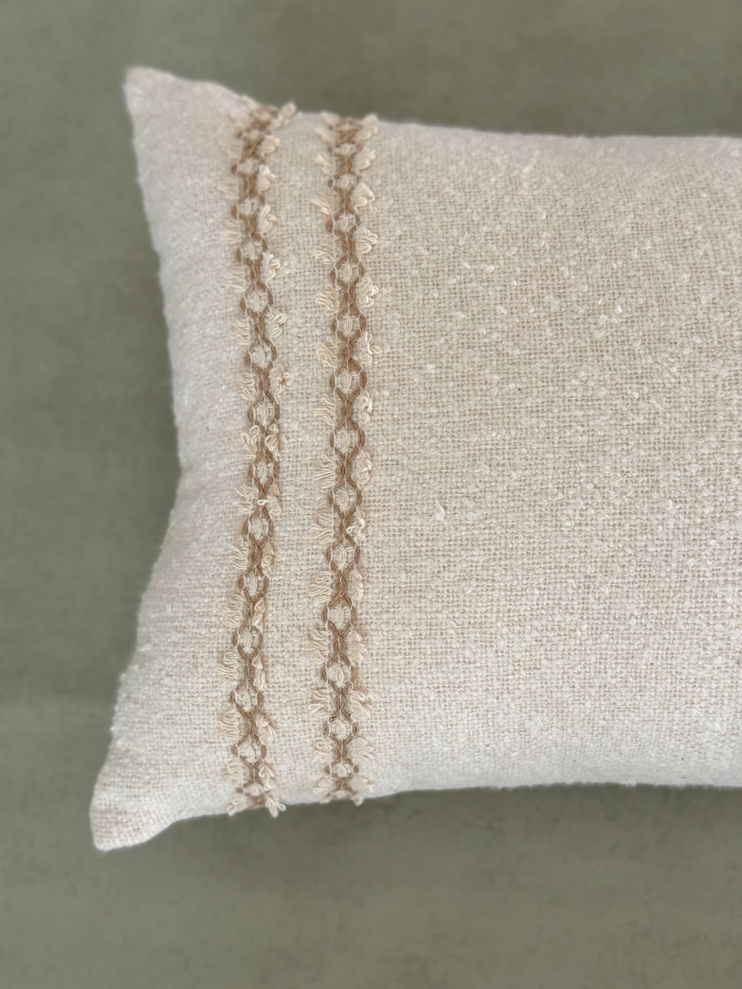 Close up of a textured ivory oblong cushion with decorative lace.