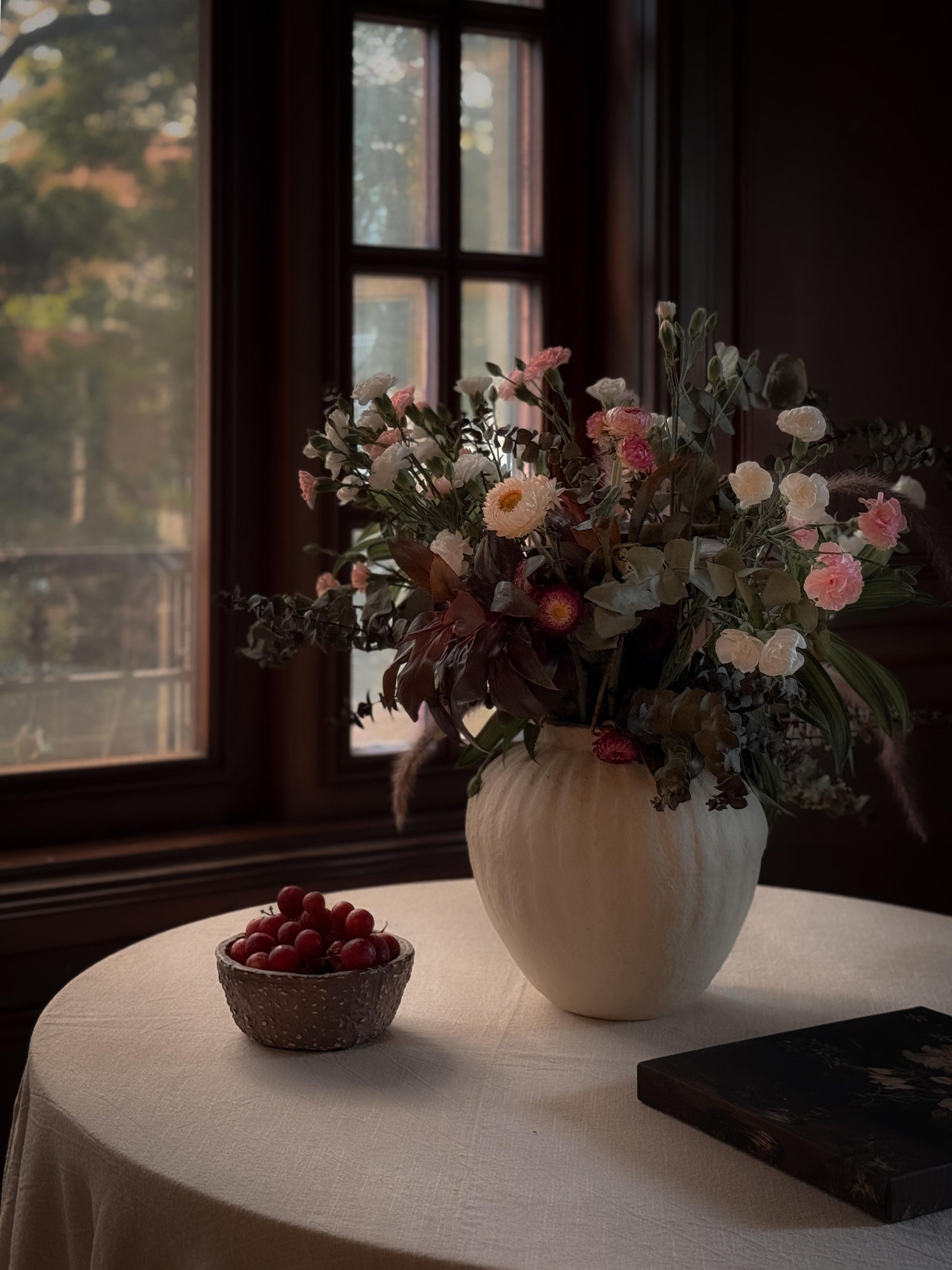 A grey round shaped and unique paper mache textured bowl styled with a flower vase for a table setup.