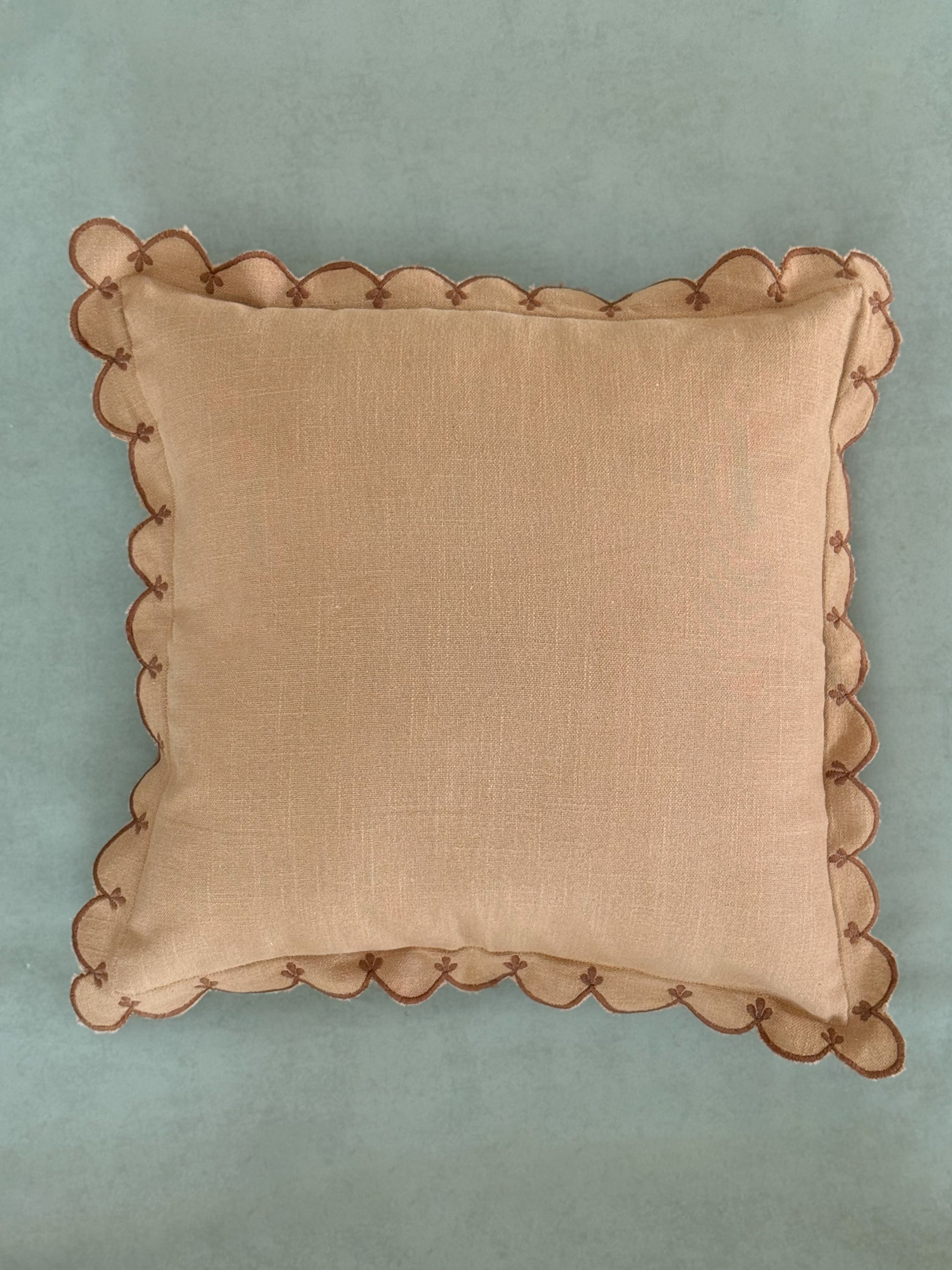Brown cushion with curved, wave-like scalloped edge detailing.