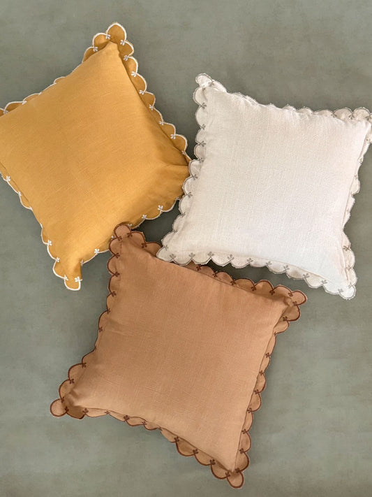 Decorative cushions in yellow, ivory, and brown with curved, wave-like scalloped detailing.
