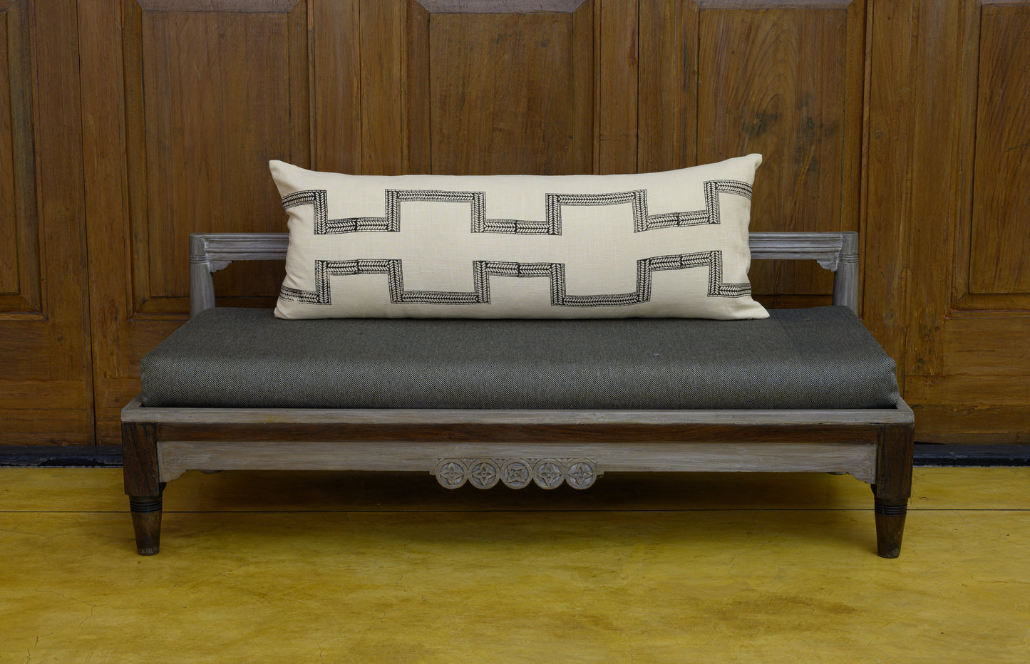 Hand block printed extra long lumbar cushion cover on a bench in a charcoal colour on an ivory cotton fabric