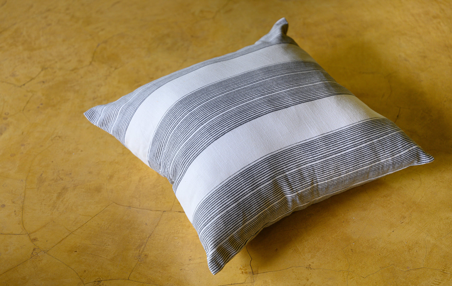 Lifestyle shot of a Block printed charcoal striped cushion cover on a mustard floor